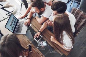 A group of young people with gadgets and a laptop arrange a brainstorm and communicate with each other. The concept of developing a young business photo