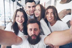 A group of people make a selfie photo in a cafe. The best friends gathered together at a dinner table eating pizza and singing various drinks