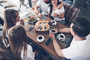 Tasty pizza on the table, with a group of young smiling people resting in the pub photo