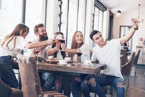 un grupo de personas hace una foto selfie en un café. los mejores amigos se reunieron en una mesa para cenar comiendo pizza y cantando varias bebidas