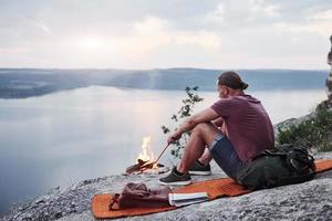 Successful man hiker on top of rock with campfire. Traveling along mountains and coast, freedom and active lifestyle concept photo