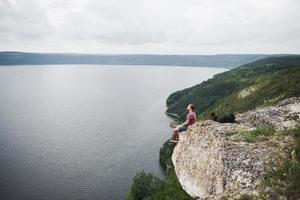 Traveller with backpack sitting on top of mountain enjoying view above the water surface. Traveling along mountains and coast, freedom and active lifestyle concept photo