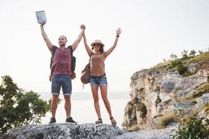 Dos turistas masculinos y femeninos con mochilas se paran en la cima de la montaña y disfrutan del amanecer. concepto de vacaciones de aventura de estilo de vida de viaje foto