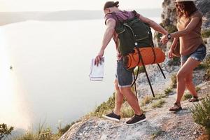 Dos turistas con mochilas suben a la cima de la montaña y disfrutan del amanecer.