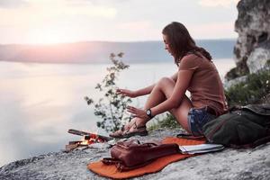 Hipster young girl with backpack enjoying sunset on peak of rock mountain. Tourist traveler on background view mockup photo