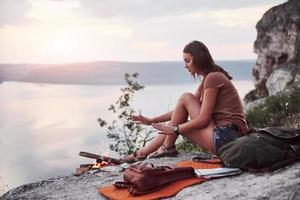 Hipster young girl with backpack enjoying sunset on peak of rock mountain. Tourist traveler on background view mockup photo