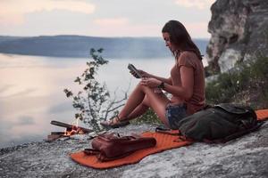 Hipster young girl with backpack enjoying sunset on peak of rock mountain. Tourist traveler on background view mockup photo