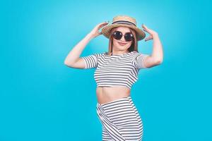 Attractive girl in a white and black stripes, hat, sunglasses, emotionally opened mouth on a bright blue background with a perfect body. Isolated. Studio shot
