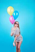 Feliz mujer sonriente está mirando en un aire globos de colores divirtiéndose sobre un fondo azul. foto