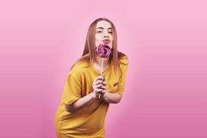 Girl cute funny portrait holding lollipop smiling on pink background. Beautiful multicultural Caucasian girl smiling happy photo