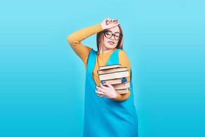 Confused cute girl holding in hands a pile of books isolated on colorful blue background photo