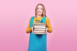 Happy cute girl holding in hands a pile of books isolated on colorful pink background.