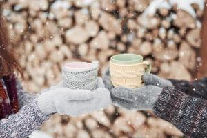 Couple hands in mittens take a mugs with hot tea in winter park photo