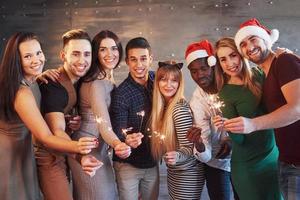 Party with friends. Group of cheerful young people carrying sparklers and champagne flutes photo