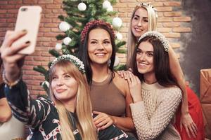 Portrait of four smiling girl with corolla on the head make selfie photo. New year's feeling. Merry christmas photo