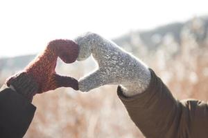 Manos de mujeres y hombres en guante dobladas en forma de corazón. concepto de invierno. nevada. foto