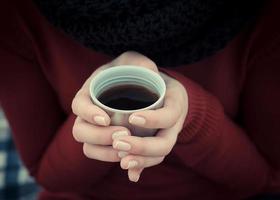 taza de café en la mano. mujer sostiene una taza de campamento con bebida caliente. foto