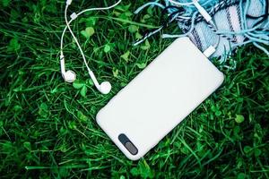 White headphones and white smartphone on green grass photo