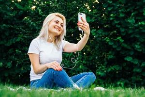 Woman in headphones and smartphone on green grass