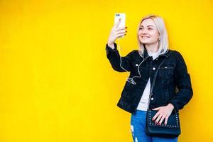 Woman in headphones and smartphone is talking on yellow wall background