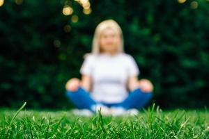Woman sitting on plaid in meditation pose on green grass
