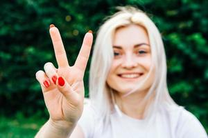 Woman shows peace sign sitting on green grass photo
