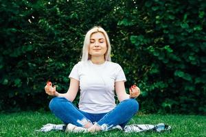 Mujer en auriculares se sienta en pose meditativa sobre la hierba verde foto