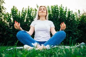 Mujer en auriculares se sienta en pose meditativa sobre la hierba verde