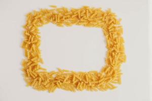 Spiral pasta on a white background forming a frame around photo