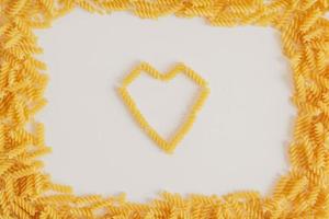 Spiral pasta in the shape of a heart and frame around on a white background photo