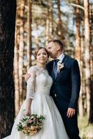 the bride and groom are walking in a pine forest photo