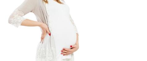 Pretty young pregnant woman standing on white background and touches the pregnant belly - cropped image.