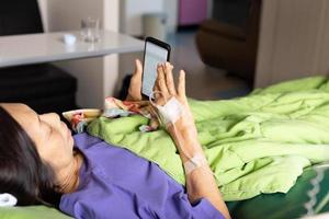 Senior patient hand with injection saline lying using cell phone in hospital. photo