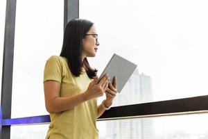 mujer de negocios que sostiene la tableta de pie junto a la ventana de la oficina. foto