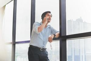 Businessman standing next to office window and talking on mobile phone. photo