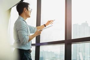 Businessman holding tablet and pointing his finger out of office window. photo