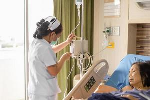 La enfermera ajusta el goteo intravenoso de líquido por goteo de solución salina para el paciente en la cama de un hospital. foto