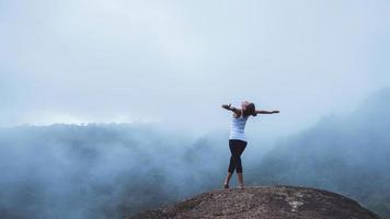 mujer joven ejercita yoga en las montañas. naturaleza de viaje de mujer asiática. viajes relajarse ejercicios yoga touch niebla natural en el pico de la montaña.