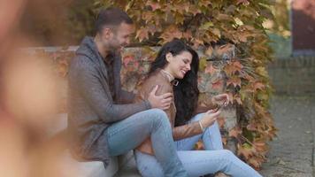 Hübsches junges Paar, das auf Außentreppen sitzt und an einem Herbsttag Handy benutzt video