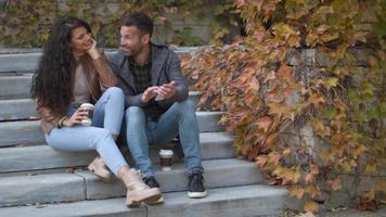 Apuesto joven pareja sentada en las escaleras al aire libre y con teléfono móvil en un día de otoño