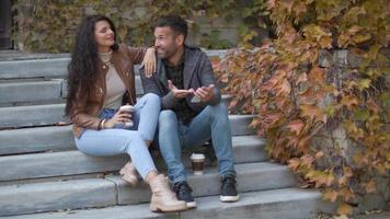 beau jeune couple assis sur des escaliers extérieurs et utilisant un téléphone portable un jour d'automne video