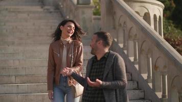 Bonita pareja joven sonriendo y hablando mientras pasea por las escaleras al aire libre en el día de otoño video