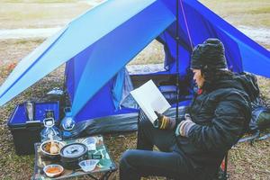 viaje de hombre asiático relajarse acampando en las vacaciones. acampar en la montaña. sentarse relajarse leer un libro en la silla. tailandia foto