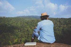 viaje de hombre asiático relajarse en las vacaciones. asientos relajarse leer libros sobre acantilados rocosos. en la montaña. En Tailandia