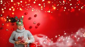 Christmas New Year. Young Woman dressed in warm sweater with  Props ball red with christmas ornaments in Holiday on shine red background. Concept merry christmas. photo