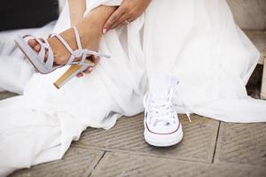 Bride changing her formal shoes with comfortable white sneakers
