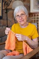 70s grandmother looking at camera enjoying knitting at home. photo
