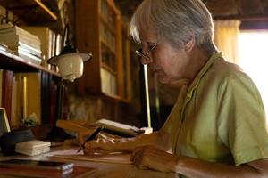 Serious mature woman in glasses writing a letter at home photo