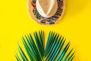 Straw hat and sunglasses with Green palm leaves on a bright yellow background. summer concept, Beach travel. photo
