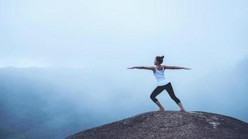 Young woman exercises yoga in the mountains. Asian woman travel nature. Travel relax exercises yoga touch natural fog on mountain peak. photo